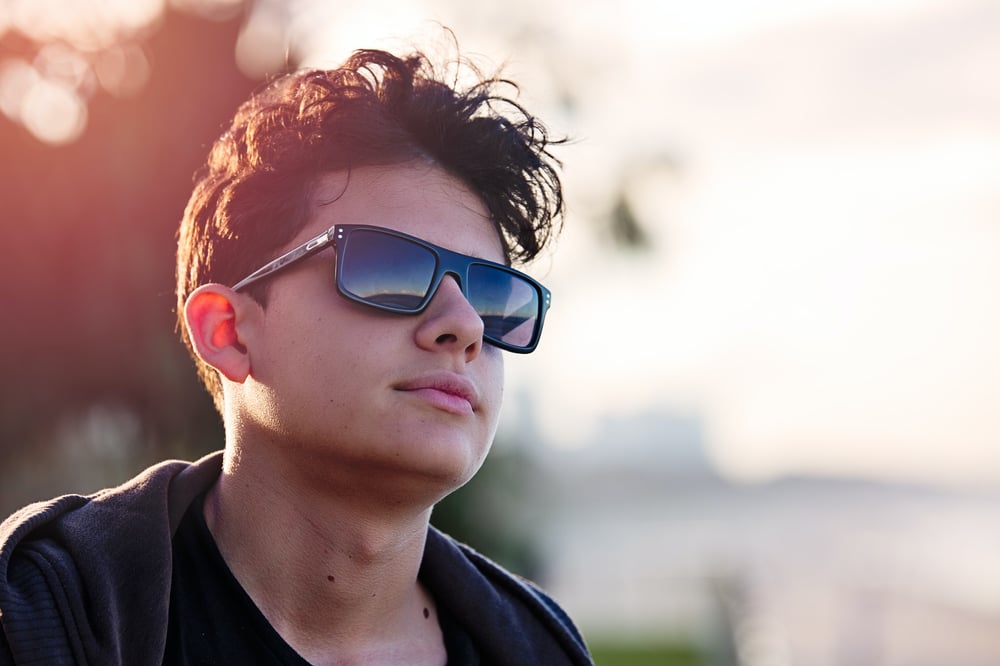 A male-presenting teenager in sunglasses looks off into the distance.