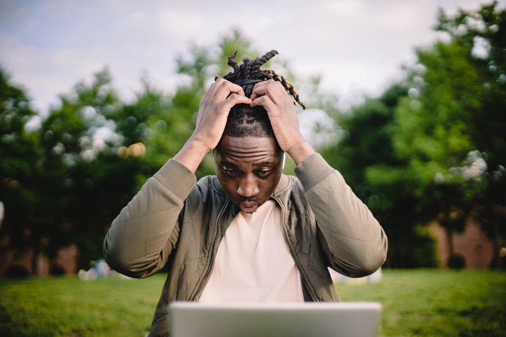 A stressed writer holds their hands in their hair while looking at their computer screen.