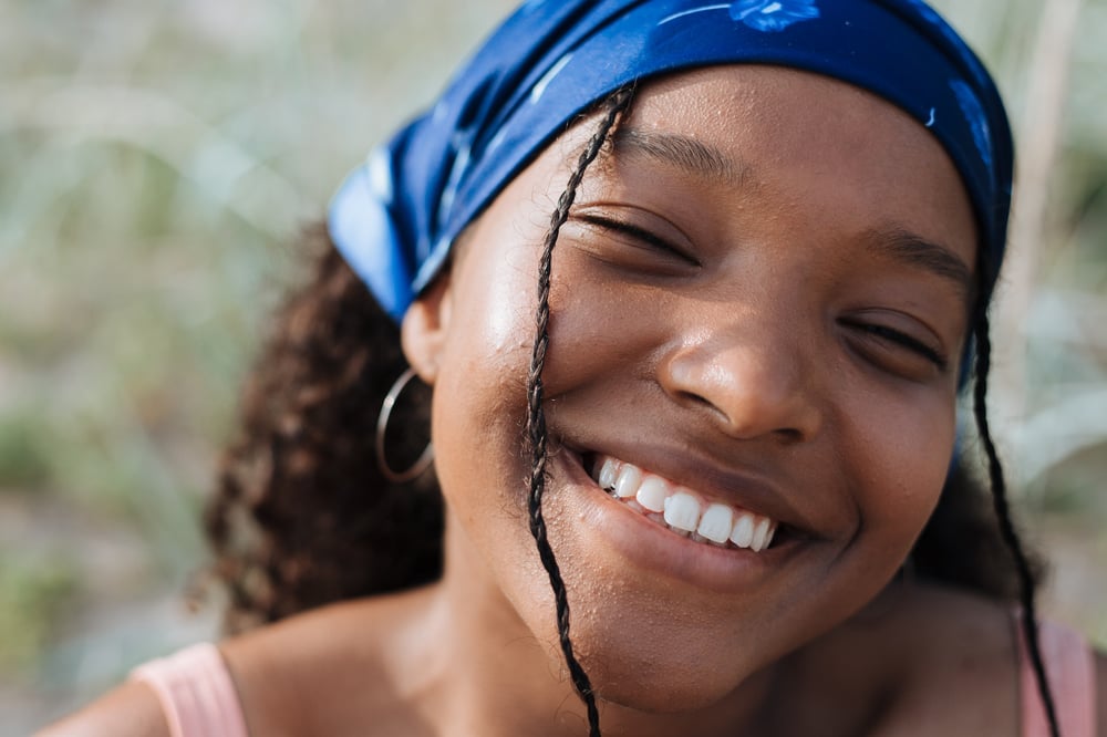 Close up of a smiling teenager with a handkerchief in their hair.