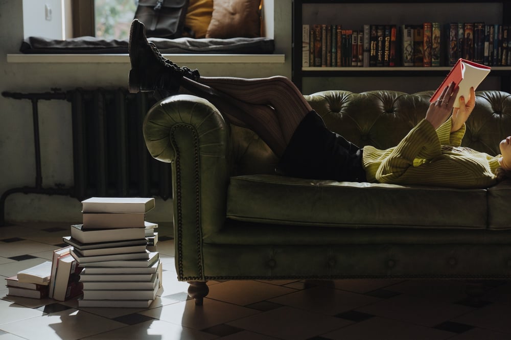 A person lies on a couch reading a book.