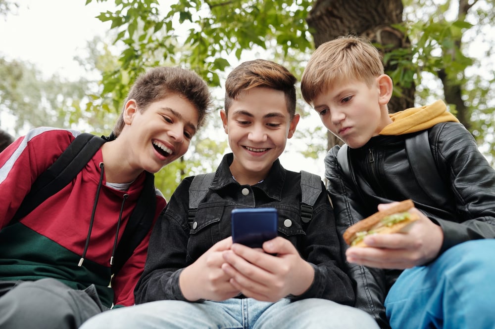 Three middle grade kids look at a smartphone together.