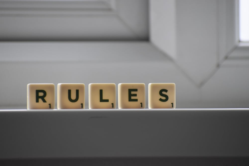 Scrabble pieces spelling out "RULES" stand on a tabletop.