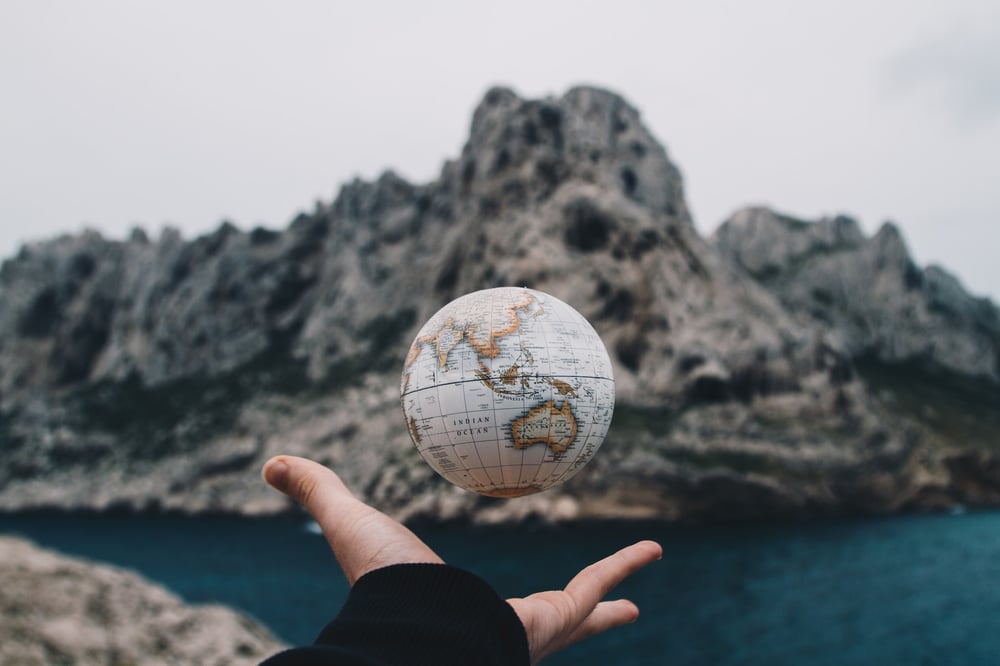 A small globe levitates over a person's open palm. A mountain and lake are in the background.