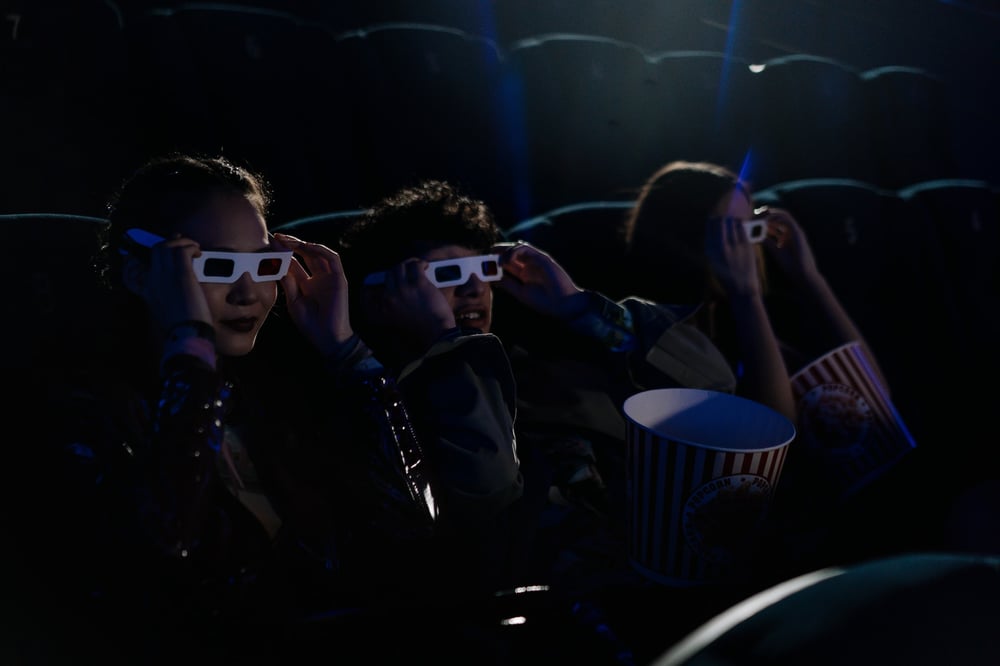 Teenagers wear 3D glasses as they watch a movie in a dark theater.