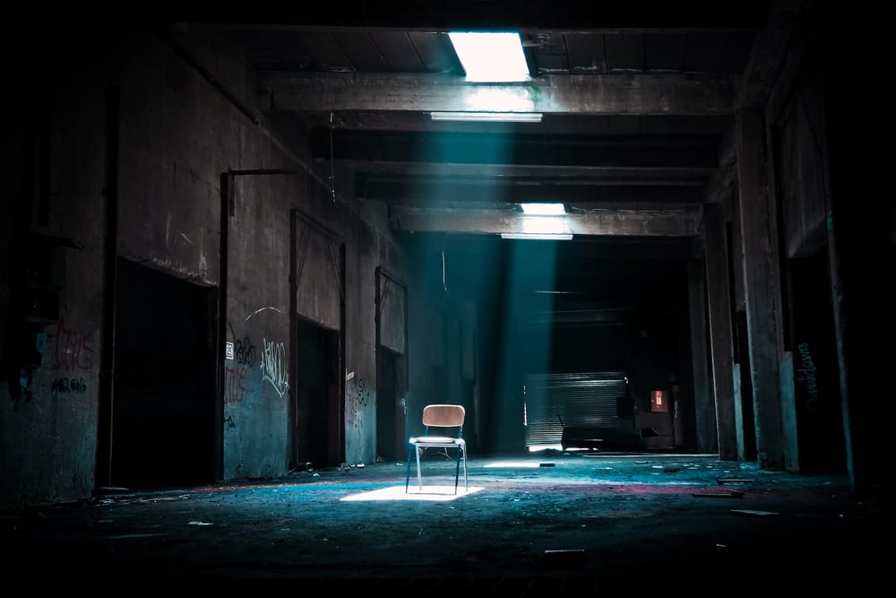 Light shines down on a single metal chair in an abandoned industrial building.