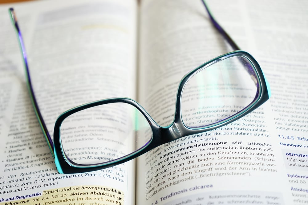 A pair of glasses sits on top of an open textbook.