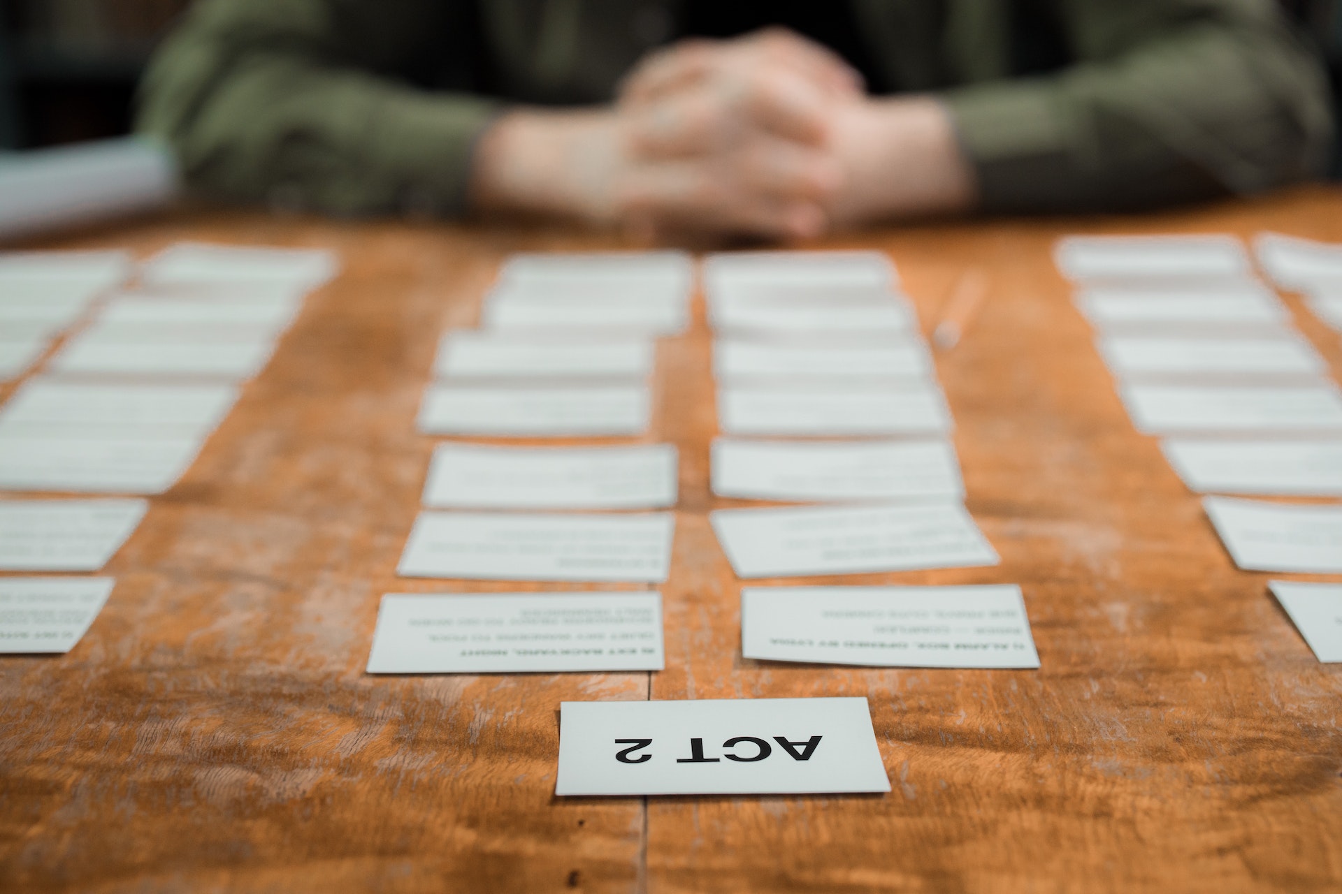 A table of scene cards spread out with a writer's hands folded on the table in the background.