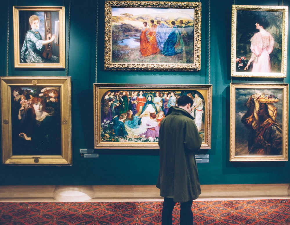 A person stands in front of a wall of paintings in a museum.