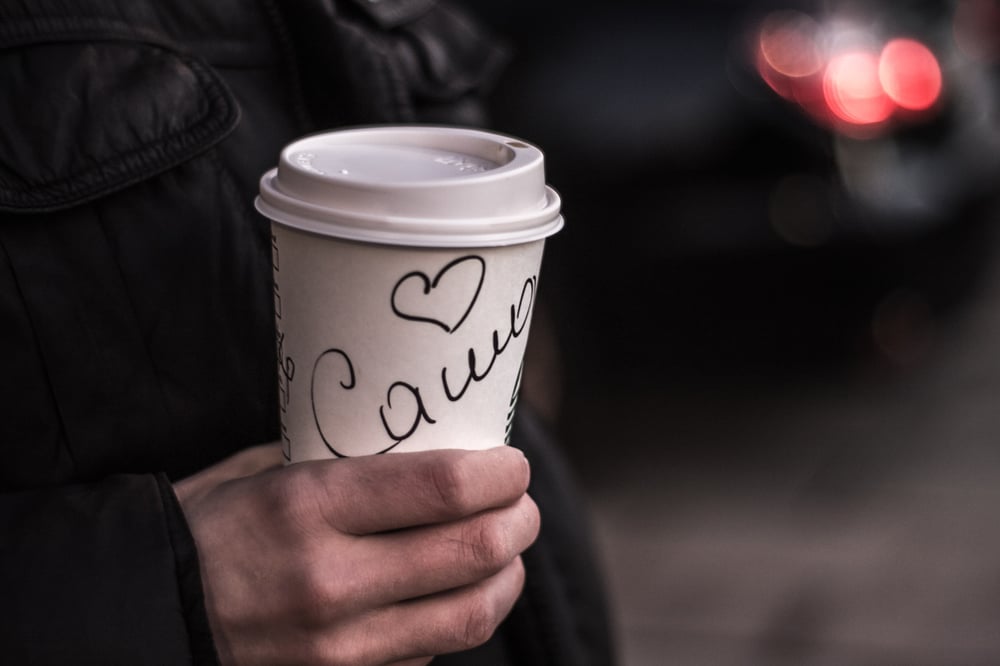 A hand holds a coffee cup with an illegible name written on it.