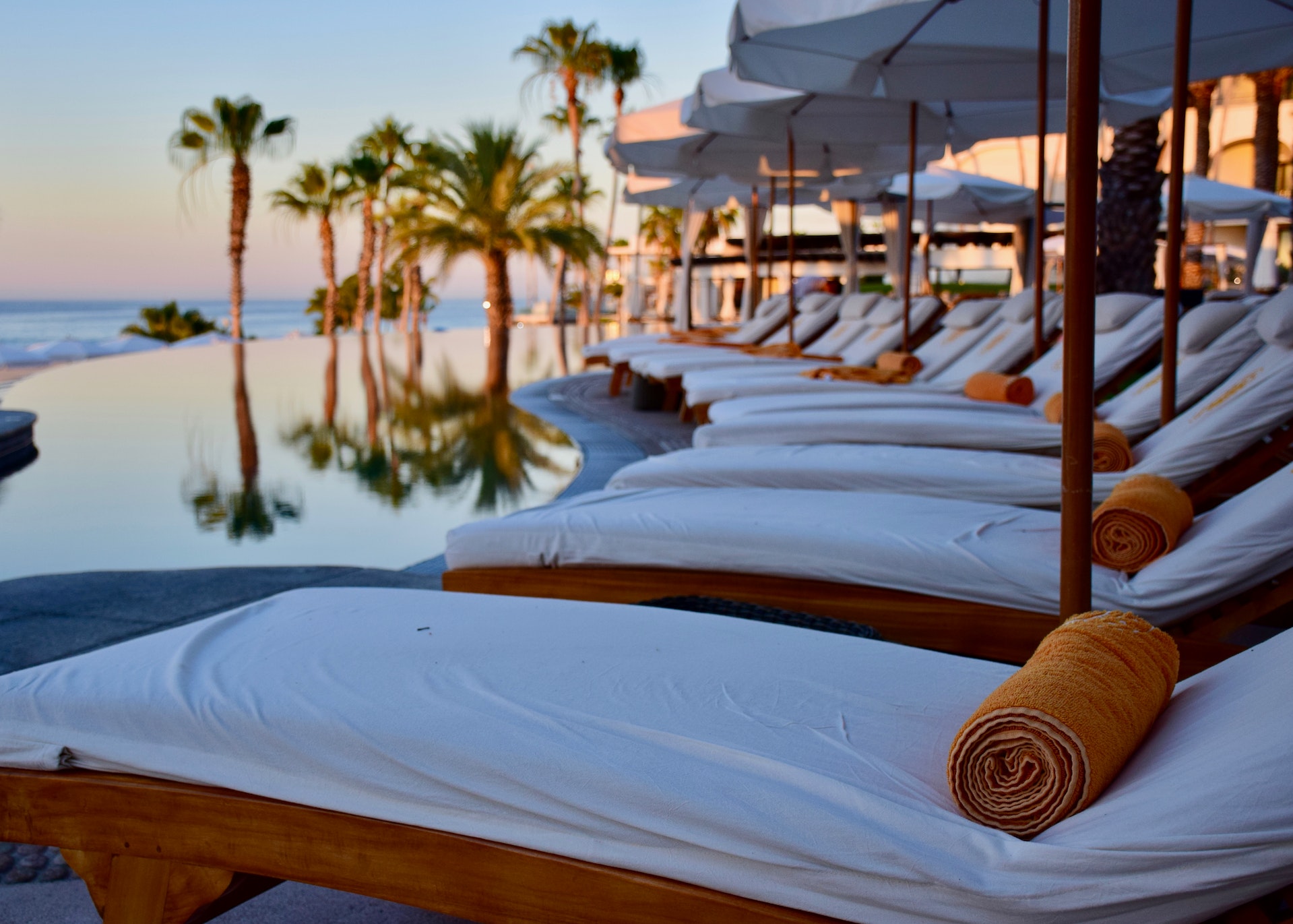A row of lounge chairs beside an infinity pool at a tropical resort.