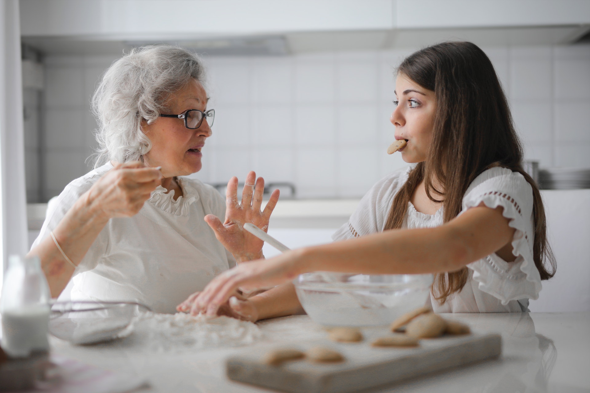 A grandmother speaks animatedly to a teenage granddaughter who has a cookie in her mouth.