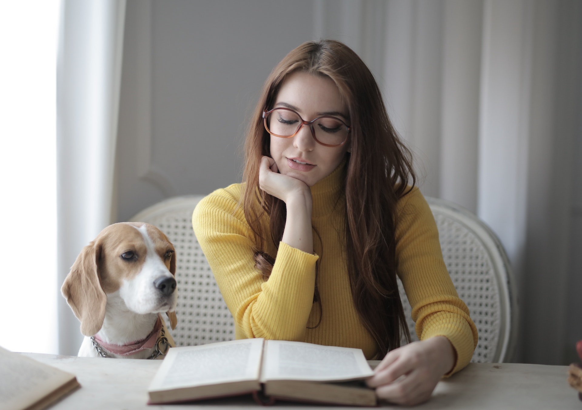 A female-presenting sits beside a dog and reads a book.