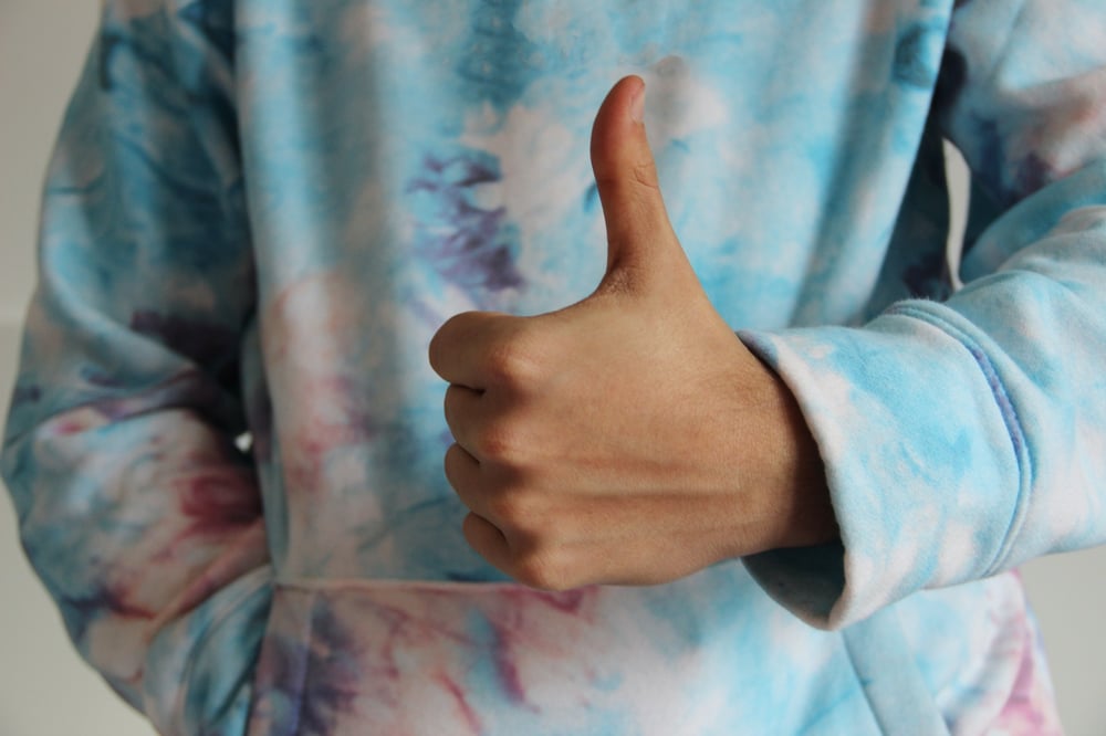 A person in a tie-dye sweatshirt gives a thumbs up.