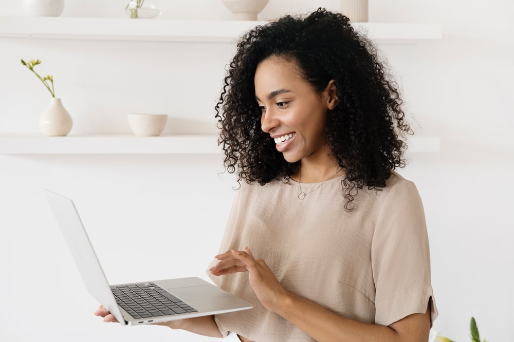 A writer holds a laptop and smiles at the screen.