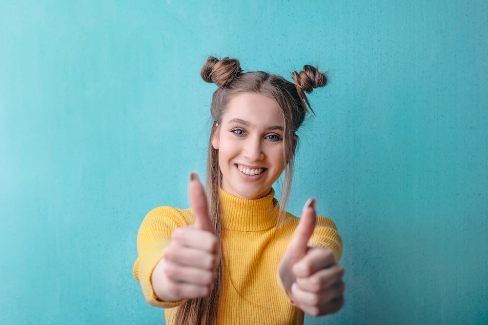 A person wearing space buns holds out two thumbs up.