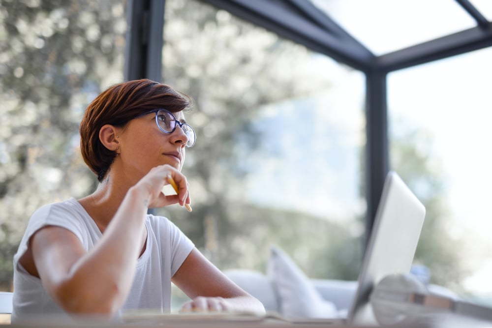 A writer sits in front of a computer and stares off into the distance, thinking.