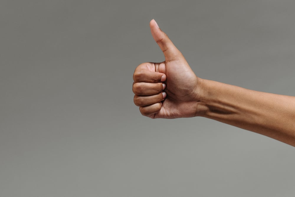 A hand gives a thumbs up against a gray background.