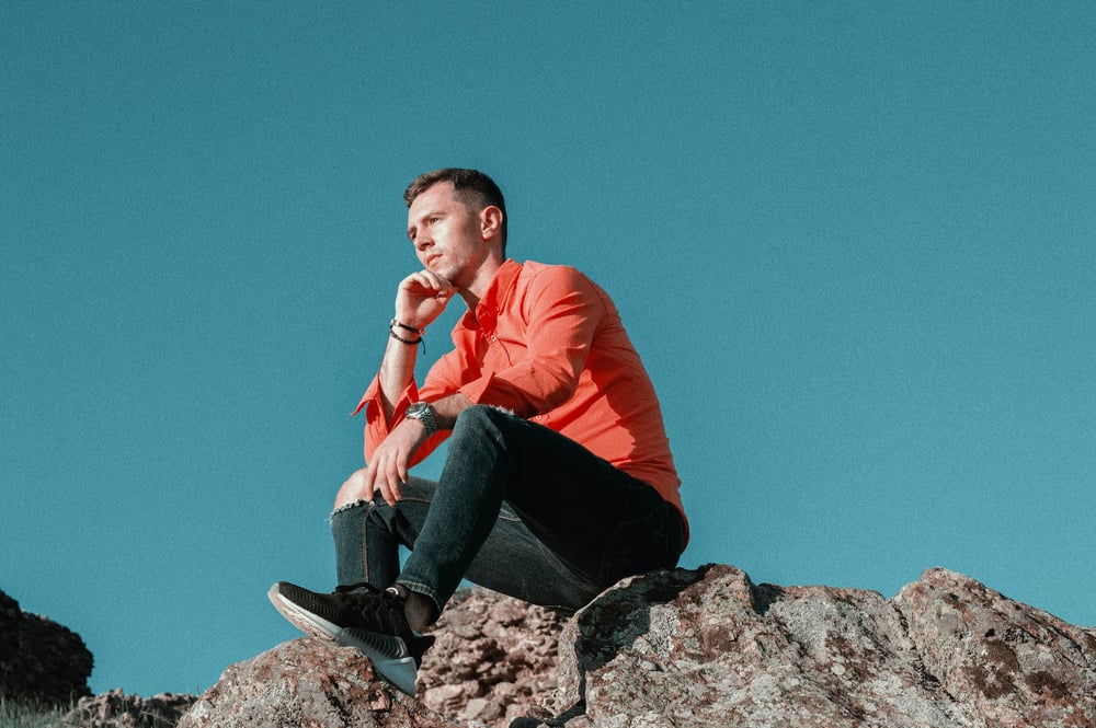 A person sits on a rock and stares into the distance, thinking.