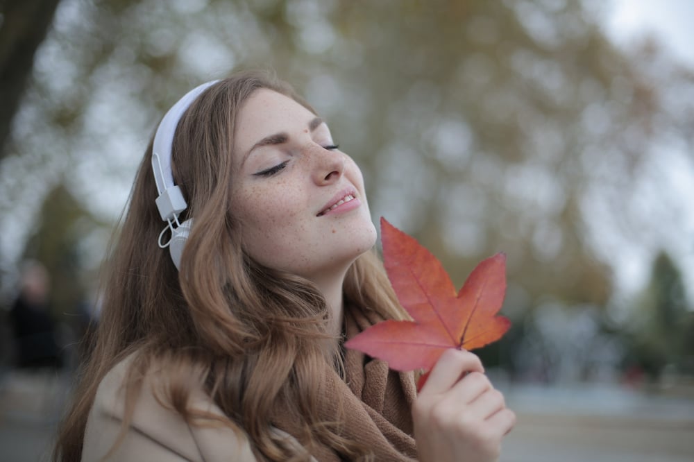 A person wearing headphones touches a red leaf to their face.