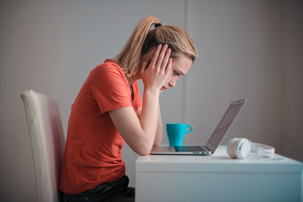 A writer holds their head in their hands and looks at a computer screen with a stressed expression.