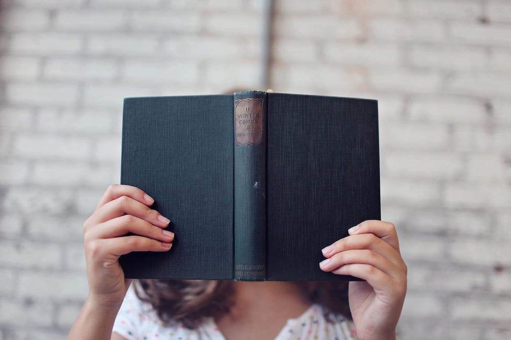 A reader holds a book in front of their face.