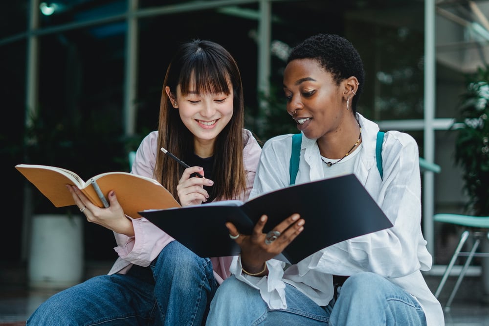 Two people smile together while looking at each other's notebooks.