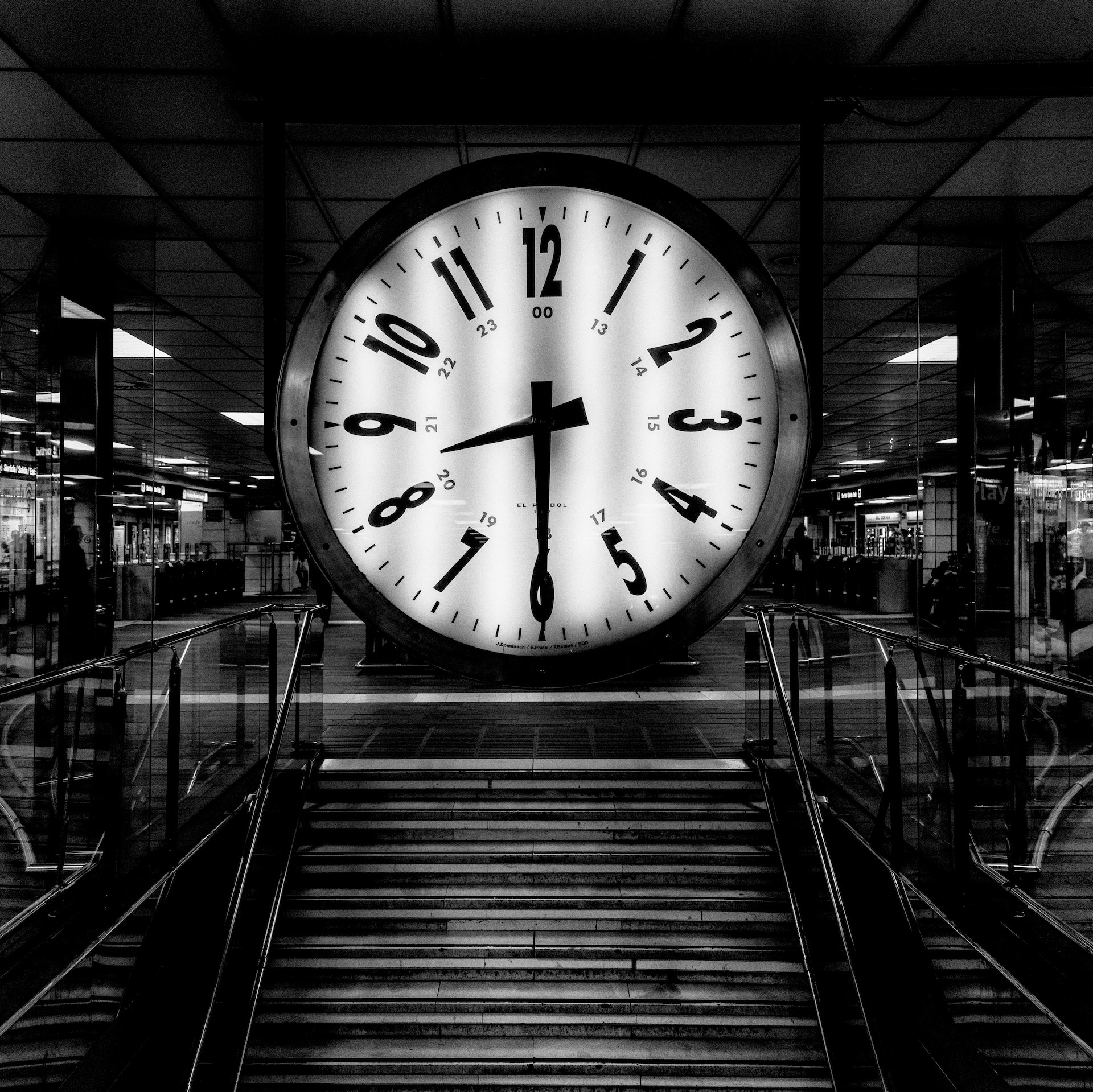 Black and white photo of a giant clock at the top of stairs.