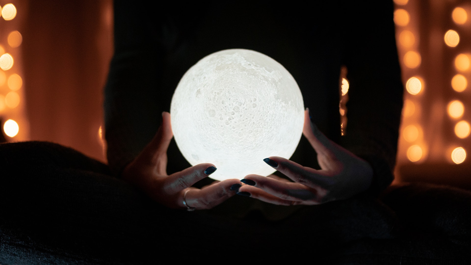 Hands hold a glowing crystal ball.