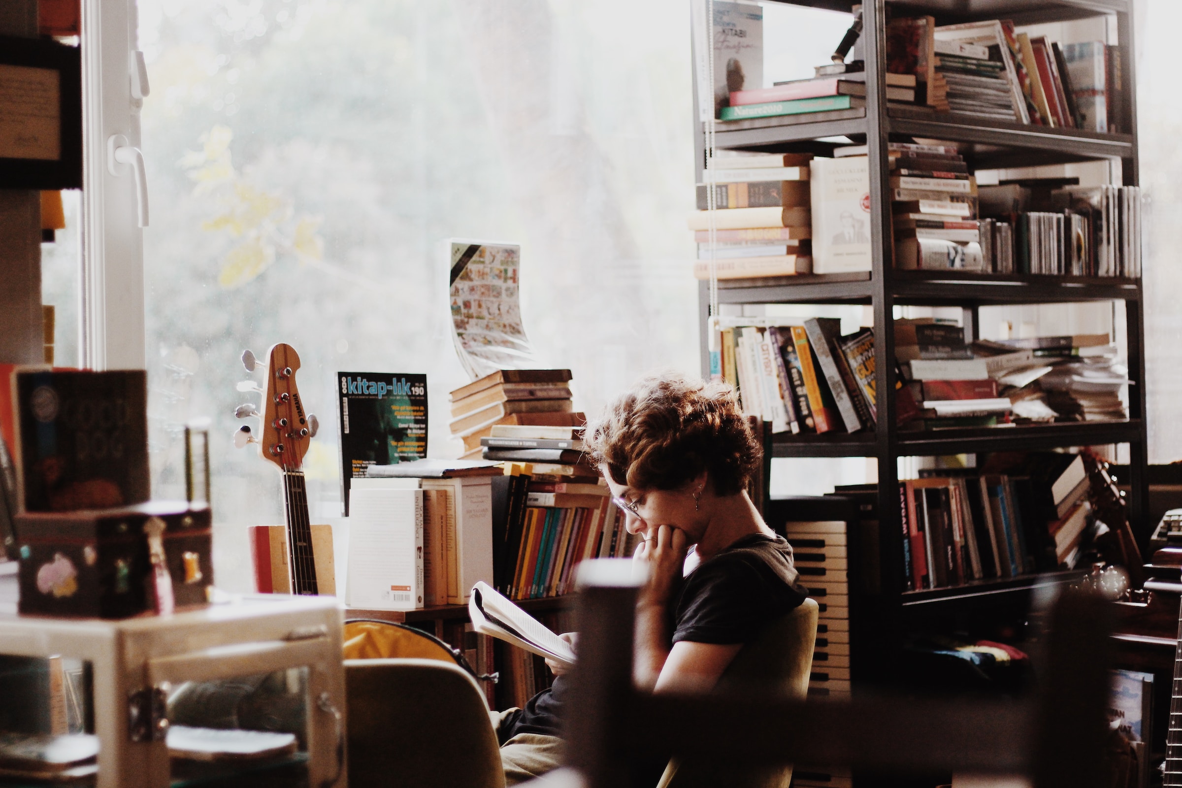 A teenager reades a book in a room full of bookshelves and musical instruments.