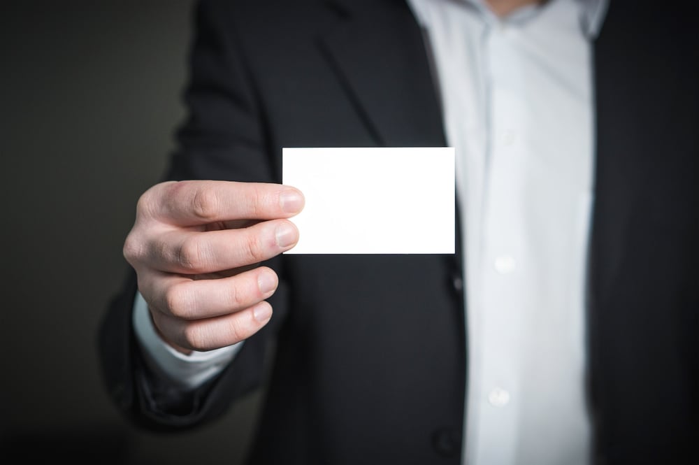 A hand holds out a blank business card.