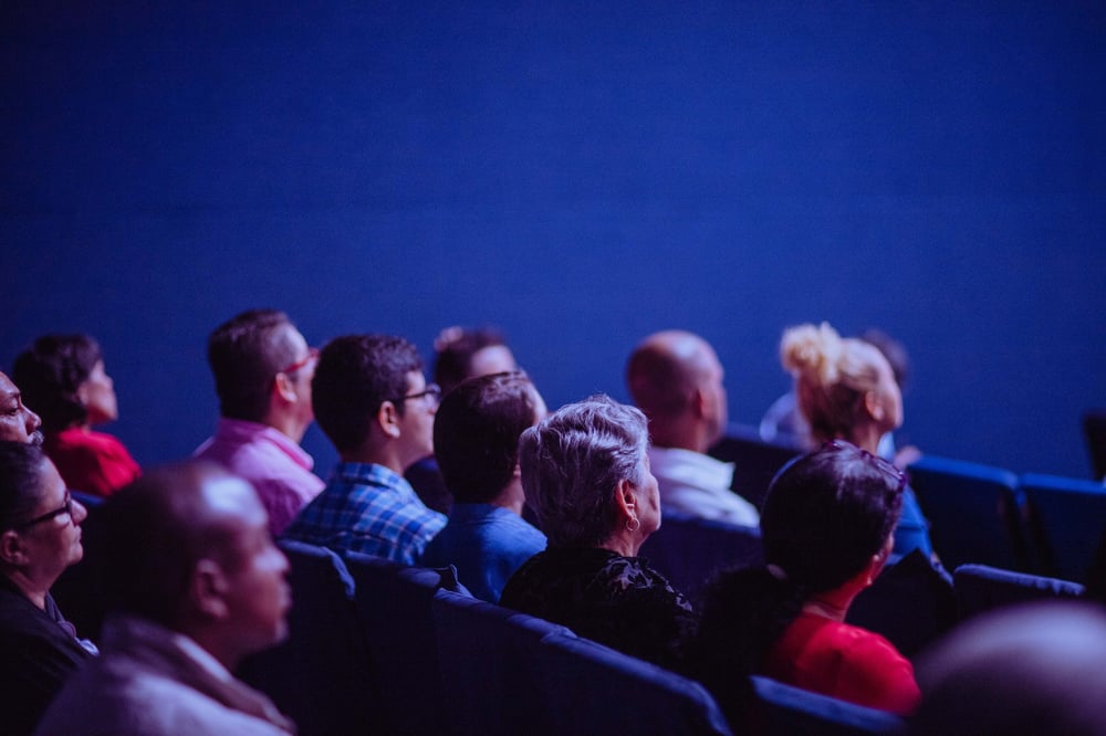 People sit in an auditorium, watching an off-camera presentation.