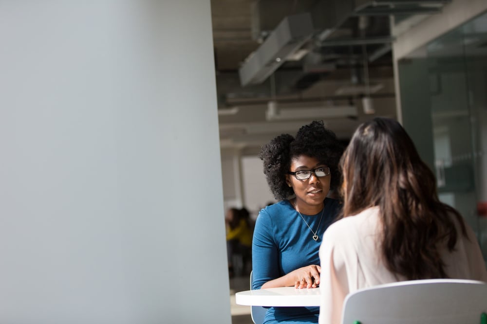 Two professionals chat at a table in a coffee shop.