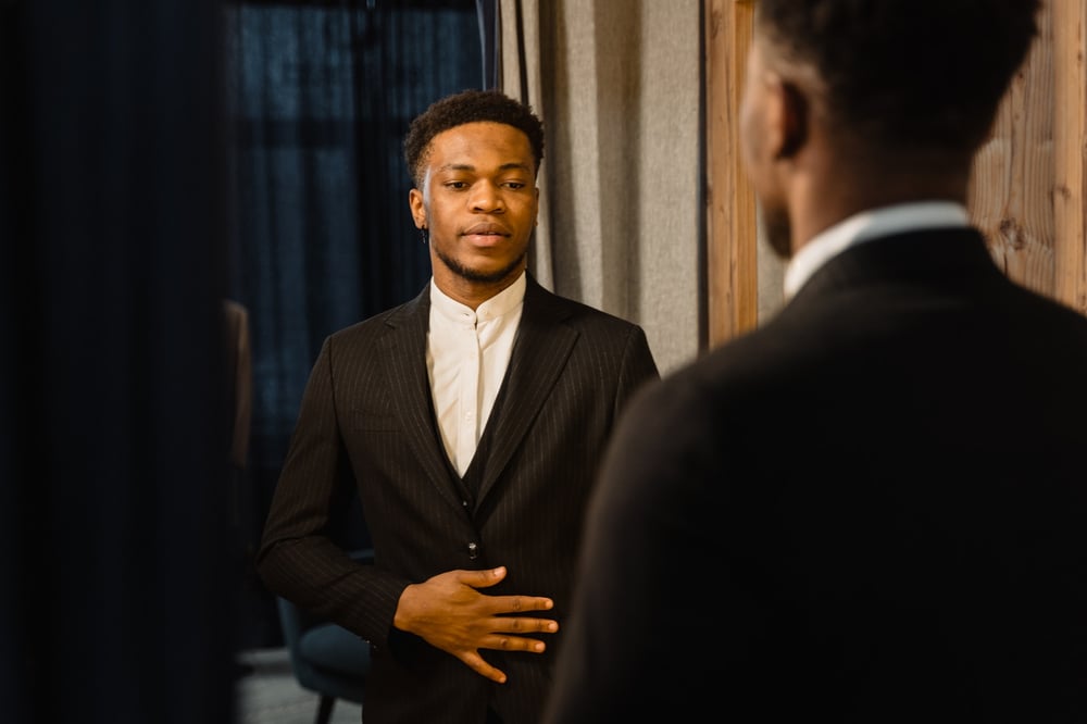 A well-dressed man looks at himself in the mirror.