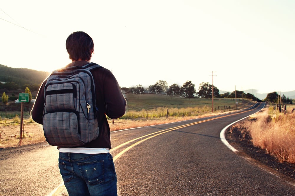 A person wearing a backpack walks down an empty road.
