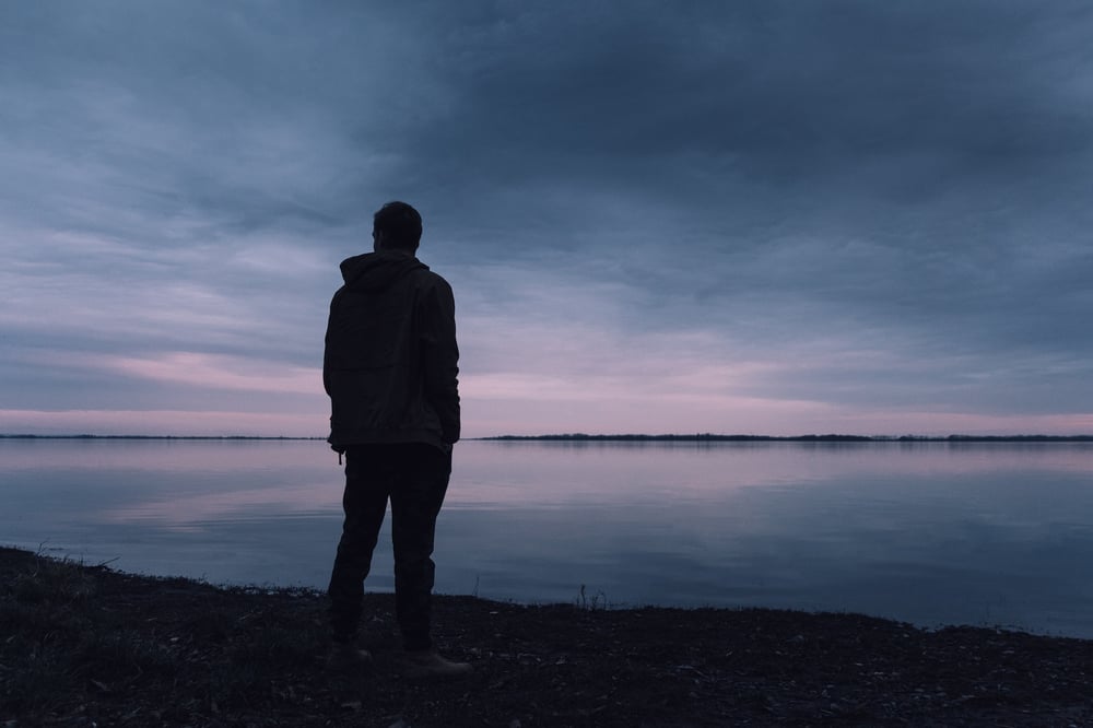 Silhouette of a person standing alone on the beach at dusk.