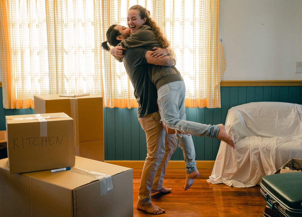 A couple hugs surrounded by boxes in their new home.