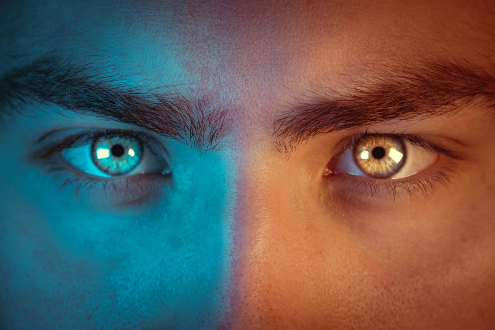 Close-up of a serious face, half lit in blue, half lit in orange.