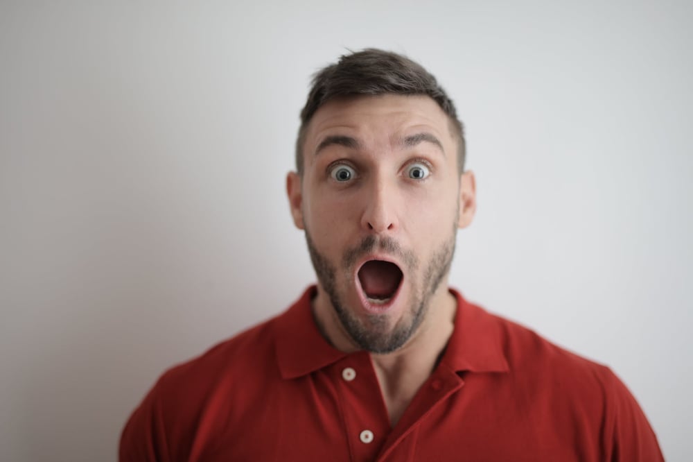 A person in a red shirt makes a surprised face.