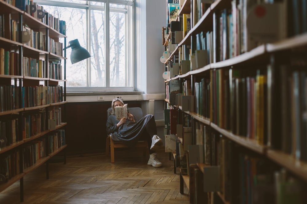 A person reads a book at the end of a row of shelves in a bookshop.