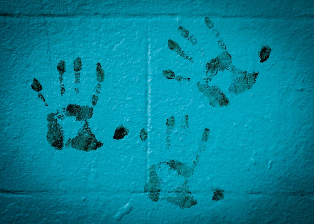 Dark handprints on a blue brick wall.