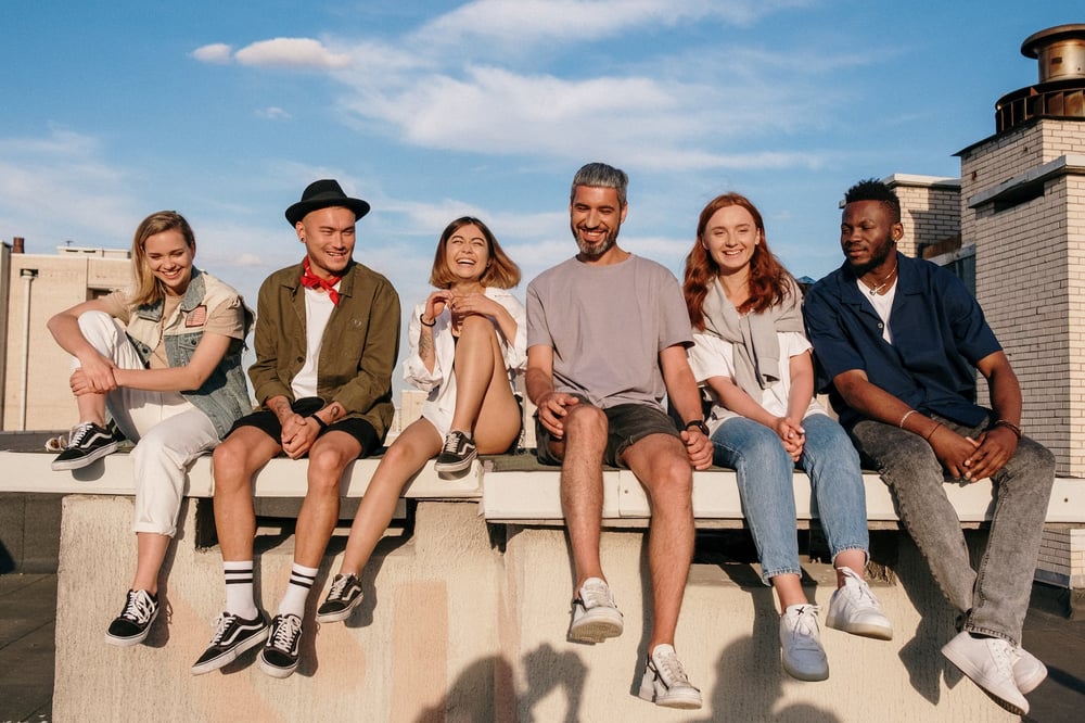 A diverse group of people sit in a row on a wall.