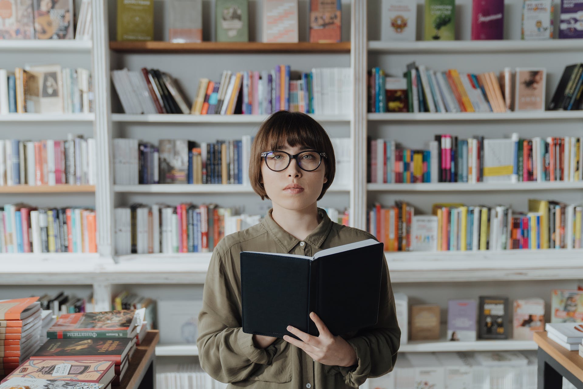 A person stands in a bookstore, holding an open book and staring straight ahead.
