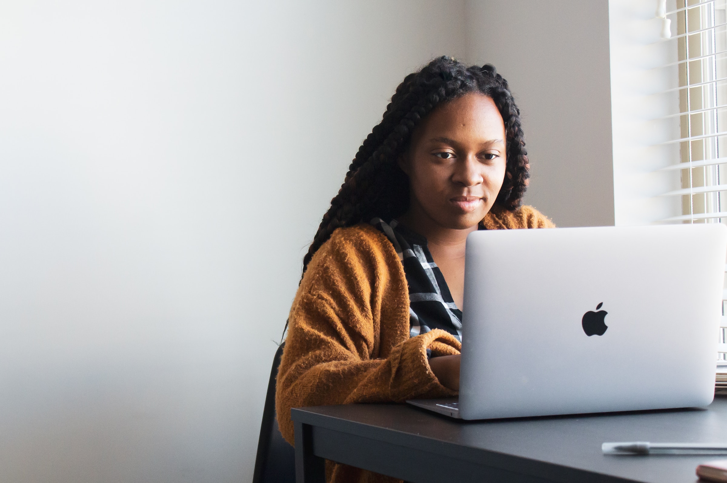 A person in an orange cardigan types on a laptop.