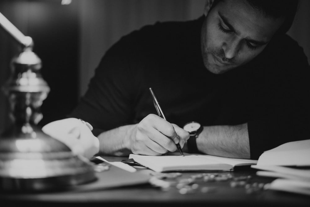 Black and white image of a writer at a desk writing in a notebook.