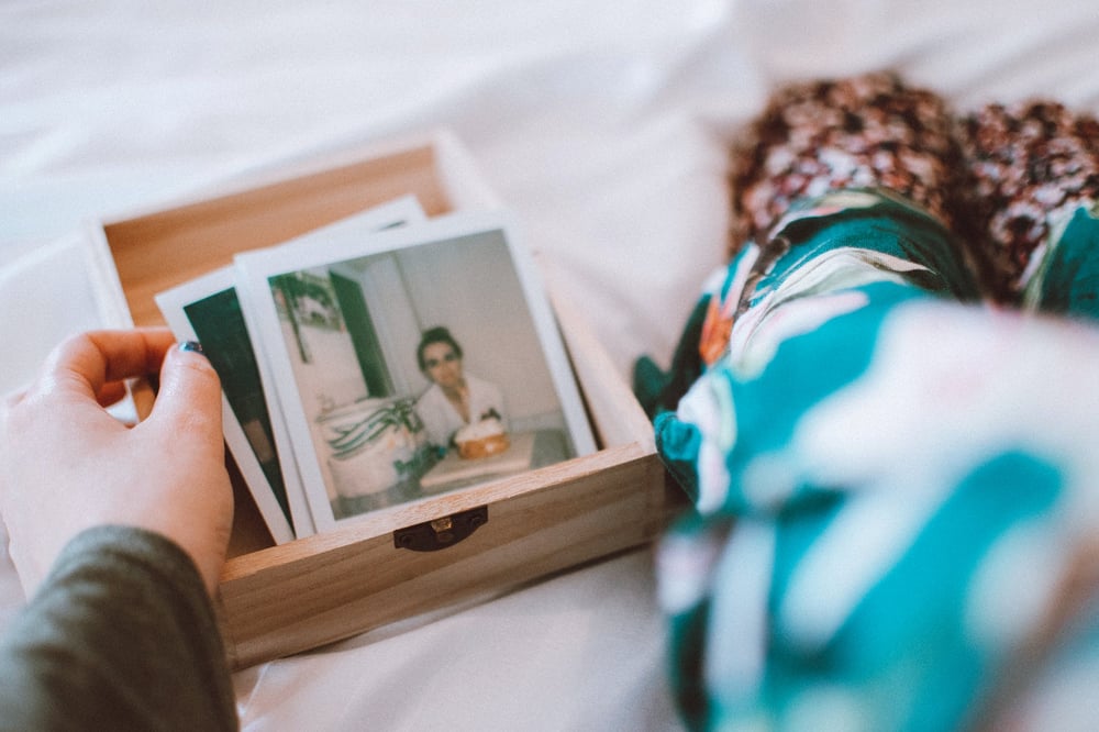 A hand pulls Poloroid photos out of a small wooden box.
