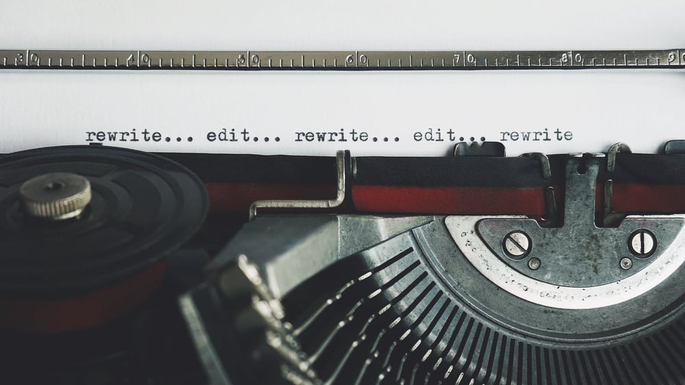 A sheet of paper in a typewriter with the words "rewrite.... edit" typed on it repeatedly.
