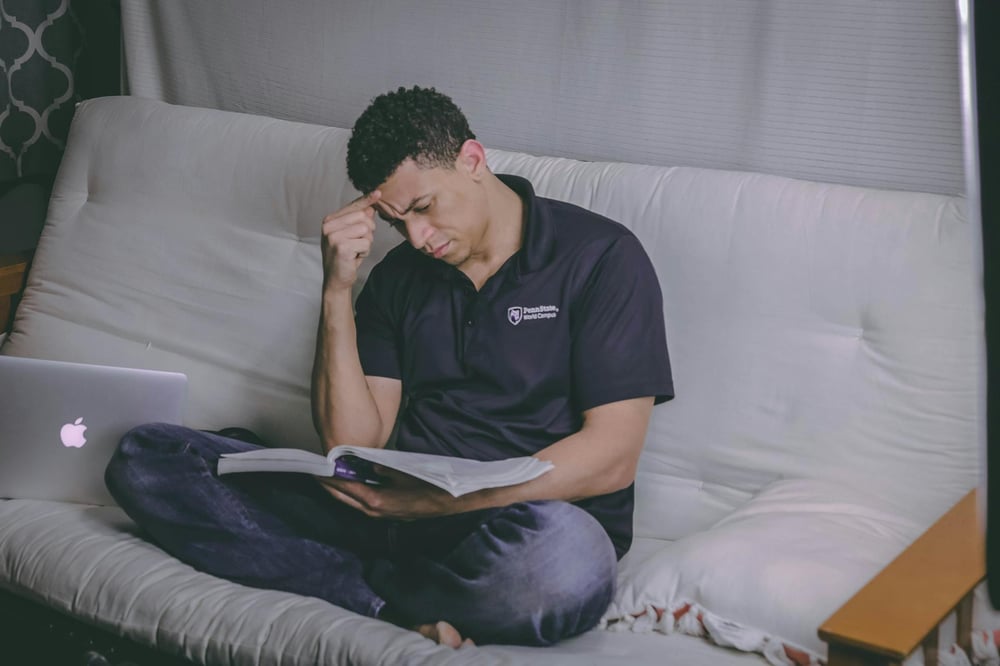 A person sits on a couch, looking very focused as they read a book.