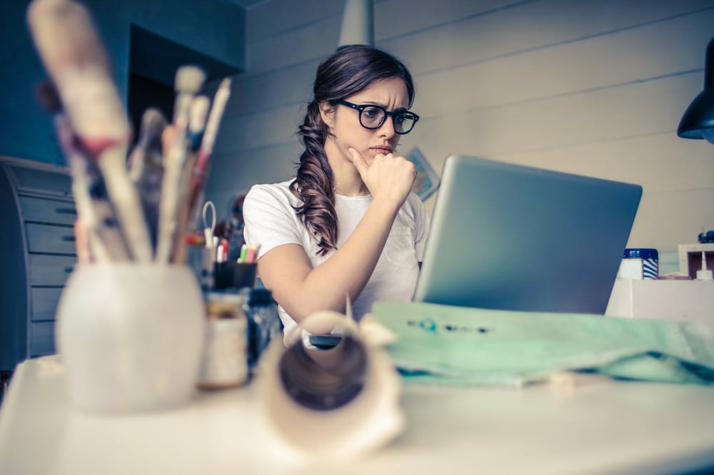 A person wearing glasses stares at a computer screen, frowning.