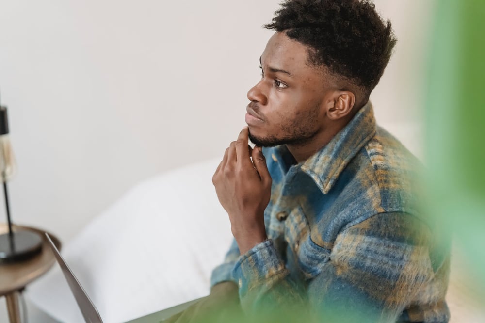 A person holds an open laptop on their lap and stares off into the distance, thinking.