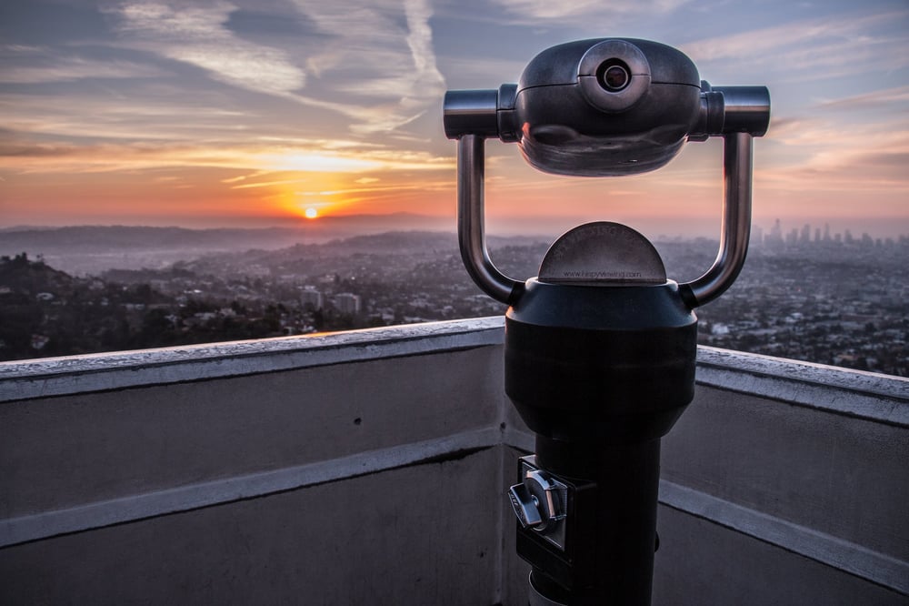 A coin-operated telescope overlooking a city by the sea.